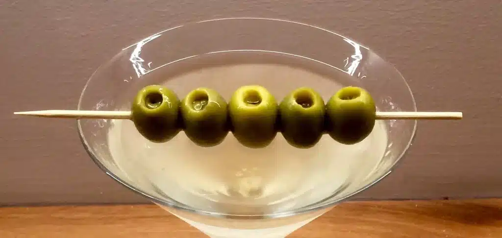 A skewer of olives laying atop a martini glass